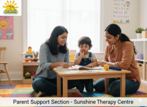 A warm and inviting therapy room with soft natural light coming through a large window. A female therapist and a female parent are sitting on the floor, smiling, at a low wooden table with a young child between them. The therapist is pointing to something in a book open on the table, while the child looks intently at the book with a finger near their mouth. A yellow microphone toy is also on the table. The room features colorful floor mats, educational posters, and shelves with toys and learning materials. In the top-left corner, the "Sunshine" logo, depicting two smiling cartoon child faces under a sun, is displayed. At the bottom of the image, there's a text overlay that reads: "Parent Support Section - Sunshine Therapy Centre."